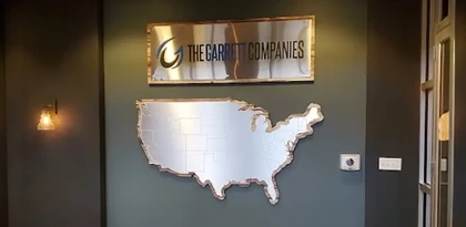 The Garrett Companies brushed metal lobby sign with dimensional lettering above a fabricated metal United States map wall installation in an Indianapolis office, created by Eye 4 Group